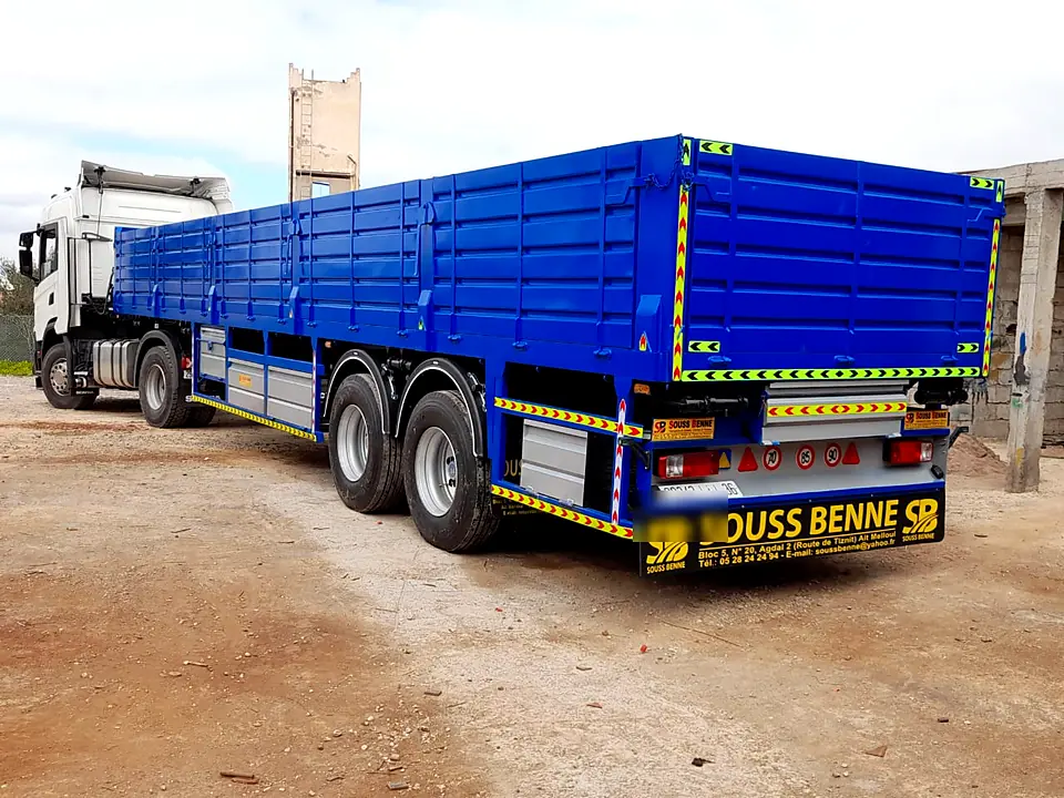 Semi-remorque à ridelles bleue avec bandes de signalisation, attelée à un tracteur, réalisation Souss Benne